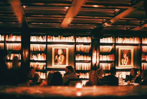 Cozy restaurant interior with bookshelves, framed art, and diners enjoying a warm atmosphere.