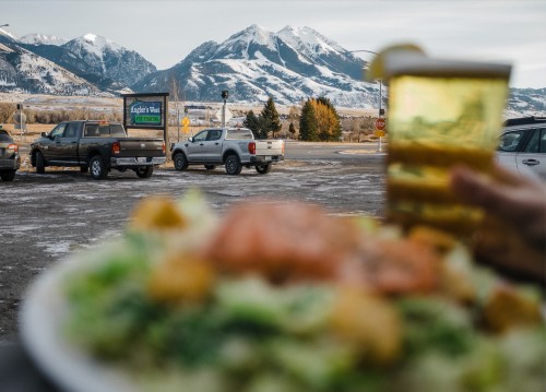 A plate of salad in the foreground with a drink, mountains in the background, and parked trucks nearby.