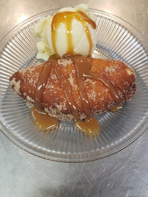 A glazed croissant drizzled with caramel sauce, served with a scoop of vanilla ice cream on a clear plate.