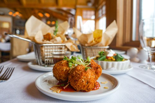 A plate of crispy fried balls on a table, garnished with microgreens, with baskets of fries and a salad in the background.