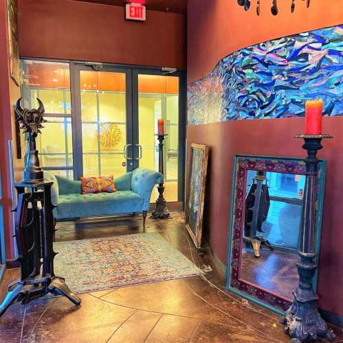 A cozy hallway with a blue couch, decorative mirrors, candle holders, and colorful wall art.