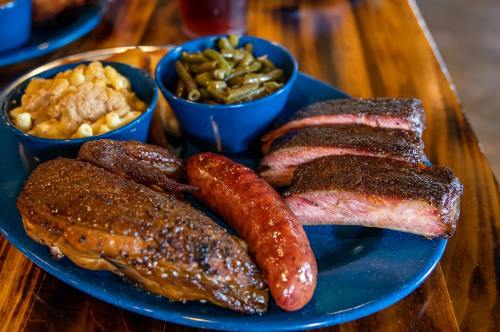 A blue plate with smoked meats, including brisket, sausage, and sides of macaroni and green beans.