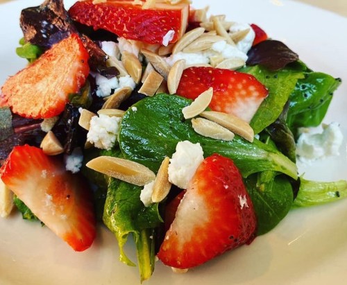 A fresh salad with mixed greens, sliced strawberries, goat cheese, and almond slivers on a white plate.
