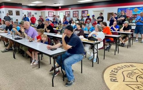 A large group of people seated at tables in a community hall, engaged in a meeting or event.