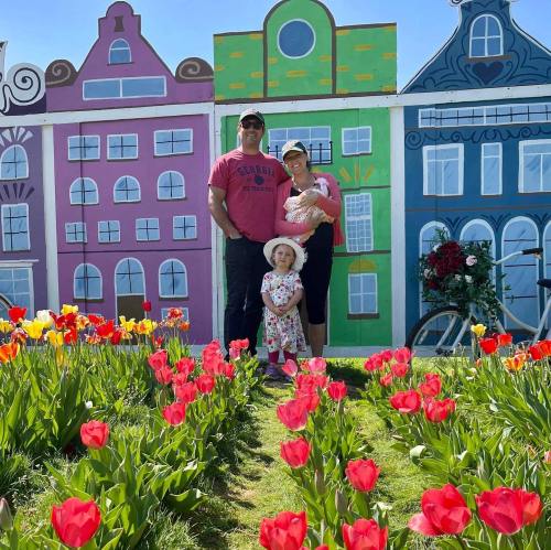 A family stands in front of colorful buildings, surrounded by vibrant tulips on a sunny day.