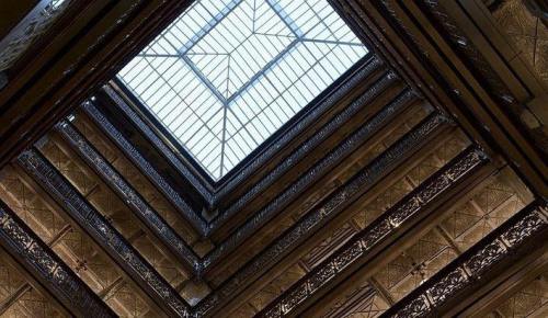 View looking up at a glass skylight surrounded by ornate architectural details and layered balconies.