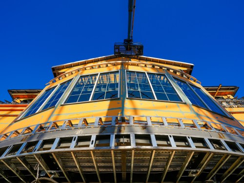 Construction of a large building with a yellow facade and large windows, under a clear blue sky.