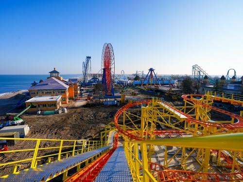 A vibrant amusement park with roller coasters and rides near a beach, under a clear blue sky.