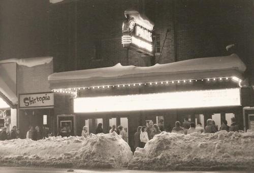 A vintage black-and-white photo of a theater entrance with snow piled outside and a crowd waiting in line.