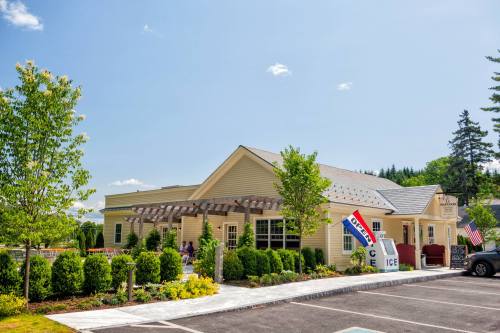 A yellow building with a porch, surrounded by greenery, featuring signs and a clear blue sky.