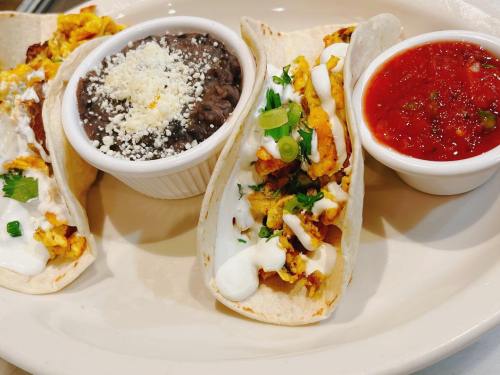 Three tacos filled with scrambled eggs, topped with sour cream and green onions, served with black beans and salsa.