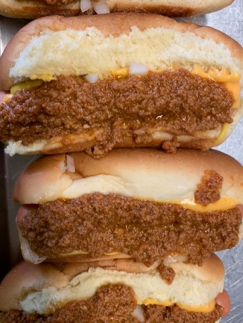 Three hot dogs topped with a thick layer of chili and melted cheese, served in soft buns.