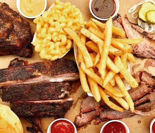 A delicious spread of barbecue ribs, brisket, macaroni and cheese, fries, pickles, and dipping sauces on a platter.