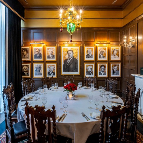 A dining room with a round table set for a meal, surrounded by framed portraits on the walls.