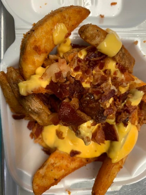 A container filled with crispy potato wedges topped with melted cheese and bits of bacon.