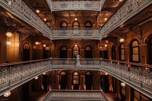 A couple stands together in a beautifully ornate, multi-level atrium with intricate railings and warm lighting.
