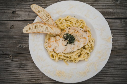 A plate of fettuccine pasta topped with grilled chicken and herbs, accompanied by two slices of toasted bread.