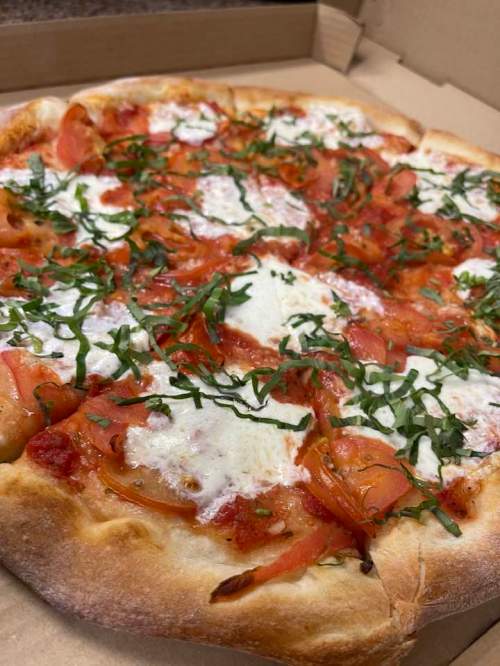 A freshly baked pizza topped with tomatoes, mozzarella, and fresh basil, served in a pizza box.