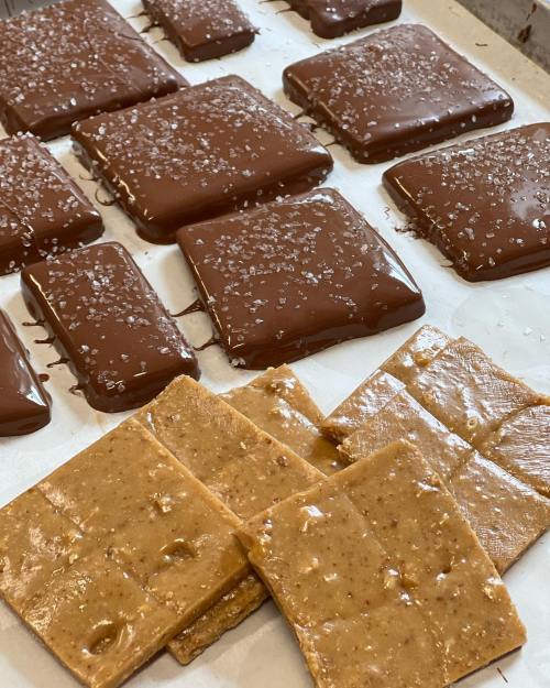 A tray of chocolate-covered treats sprinkled with sea salt, alongside pieces of caramel or nougat.