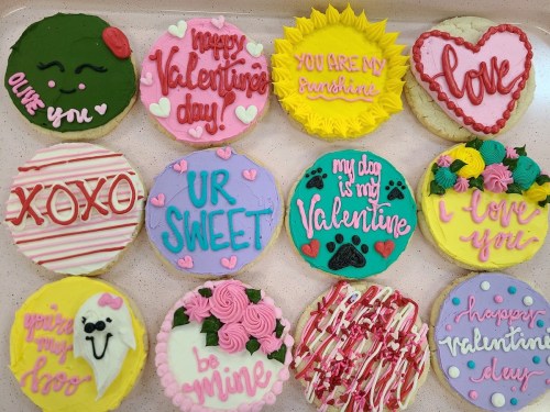 A tray of decorated cookies for Valentine's Day, featuring colorful icing and messages like "Love," "Be Mine," and "UR Sweet."