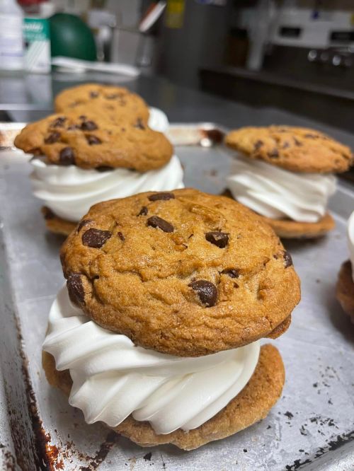 Close-up of chocolate chip cookie sandwiches filled with fluffy white cream on a baking tray.
