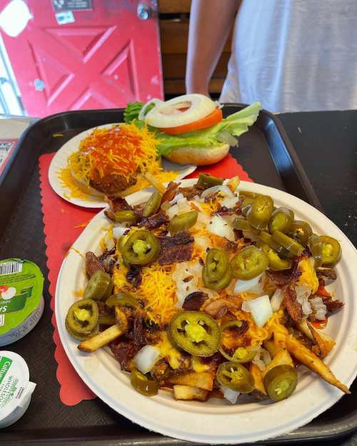 A plate of loaded fries topped with cheese, jalapeños, onions, and a side of a burger with lettuce, tomato, and cheese.
