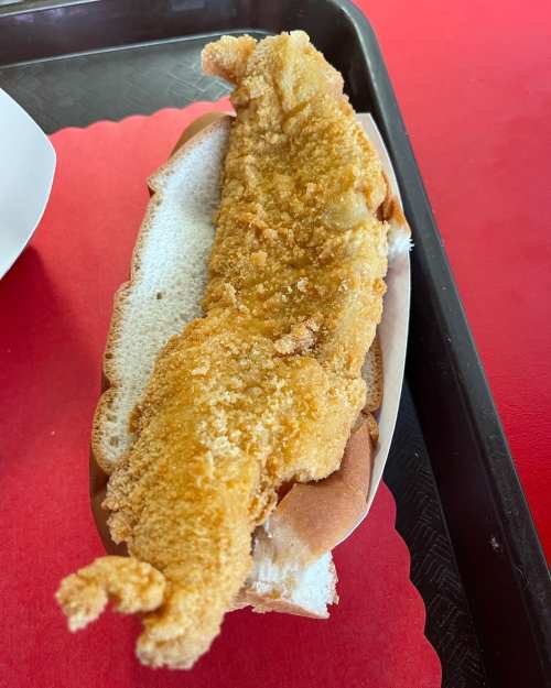 A crispy fried fish fillet served in a soft white bun on a red tray.