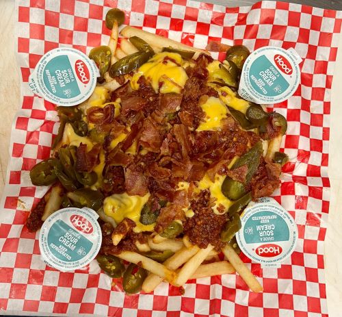 Loaded fries topped with cheese, jalapeños, and bacon, served with dipping sauces on a red and white checkered paper.