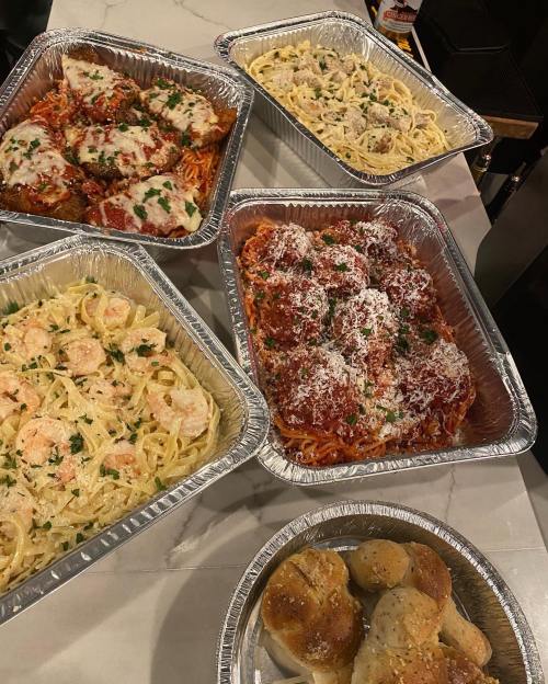 Five trays of Italian dishes: spaghetti with meatballs, chicken parmesan, fettuccine alfredo, and bread rolls.