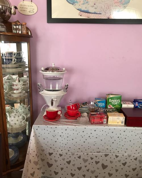 A cozy tea setup with red cups, a kettle, and various tea boxes on a table against a purple wall.