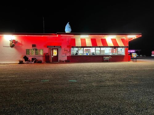 A brightly lit fast-food restaurant at night, featuring red and white stripes and a large sign on the roof.