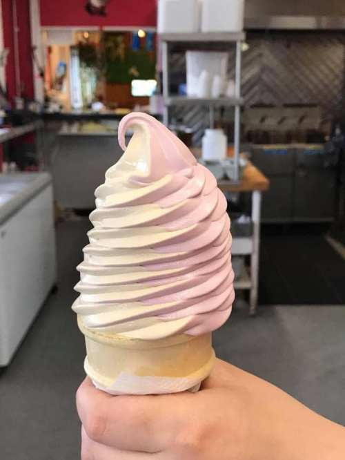 A hand holding a soft-serve ice cream cone with swirls of pink and white.