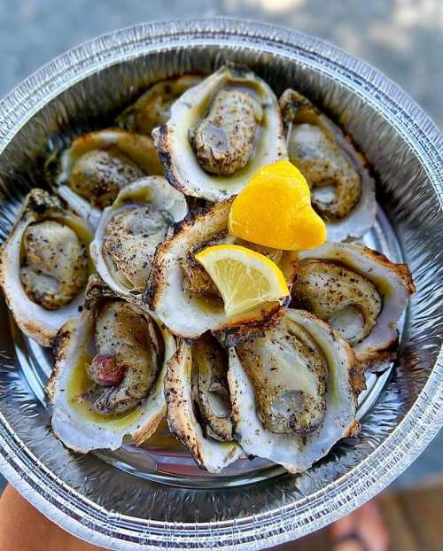 A platter of grilled oysters garnished with lemon slices and a lemon wedge on top.