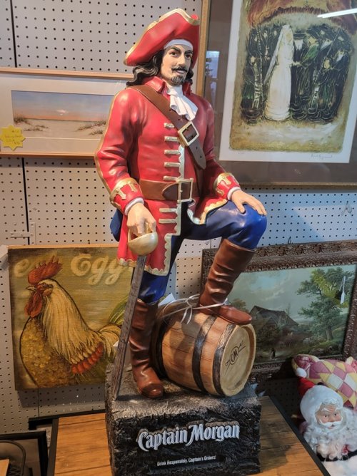 A colorful Captain Morgan statue in a pirate outfit, standing on a barrel with a hand on his knee.