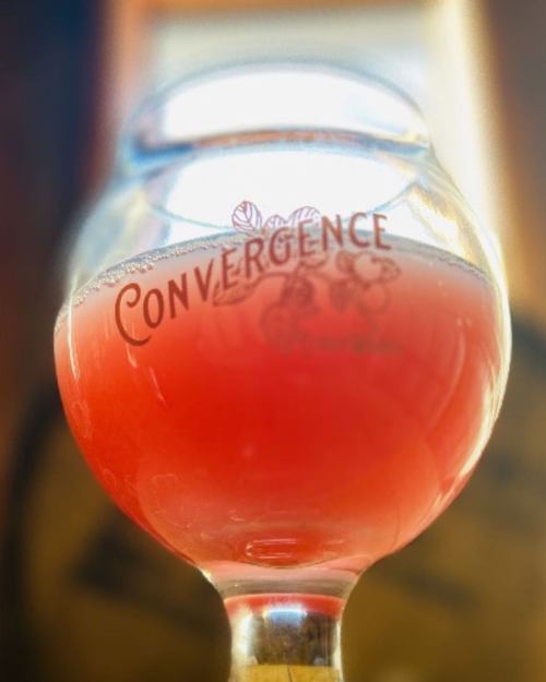 A close-up of a glass with the word "Convergence" etched on it, filled with a pinkish beverage.