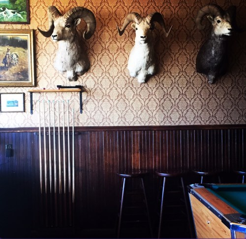 A rustic interior featuring mounted ram heads on the wall, a pool table, and wooden bar stools.