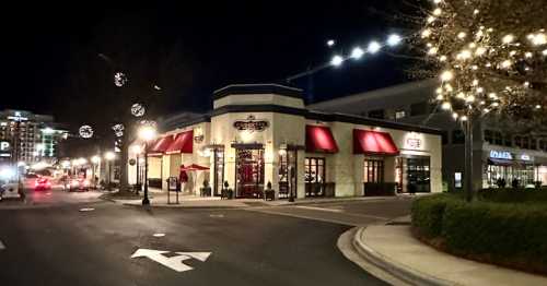 A brightly lit restaurant at night, adorned with festive lights, located at a street intersection.