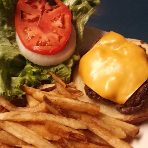 A cheeseburger with lettuce, tomato, and onion, served with a side of golden French fries.