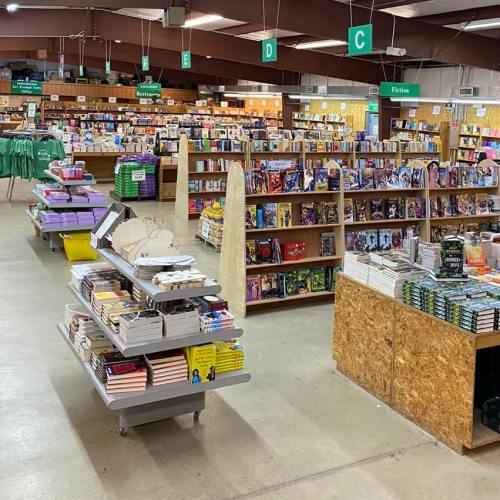 A spacious bookstore interior with shelves of books, tables of merchandise, and clear signage for different sections.