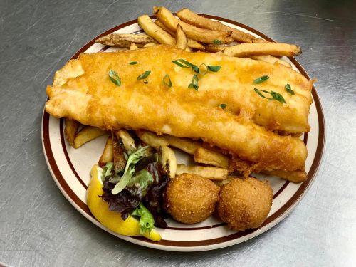 A plate of golden fried fish fillet with fries, a lemon wedge, salad, and two hush puppies.