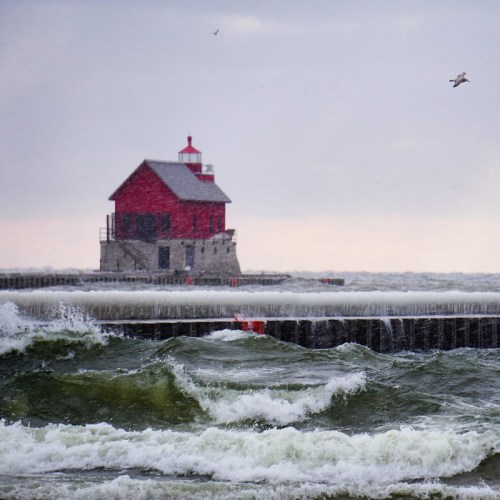 A red lighthouse stands on a pier, surrounded by turbulent waves under a cloudy sky. Seagulls fly above.