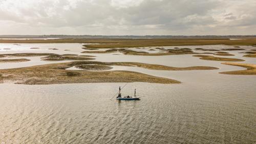 A lone boat glides through a serene marsh landscape with rippling water and grassy patches under a cloudy sky.