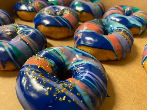 Colorful donuts with blue and pink icing, decorated with glitter, arranged on a tray.