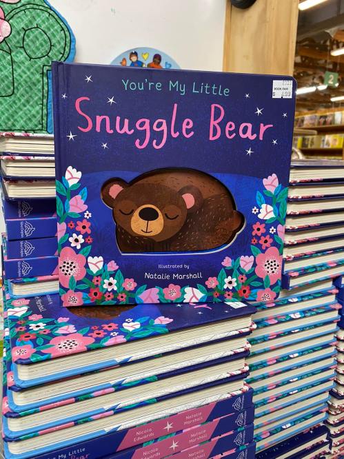 A children's book titled "You're My Little Snuggle Bear" with a sleeping bear illustration, displayed among other books.