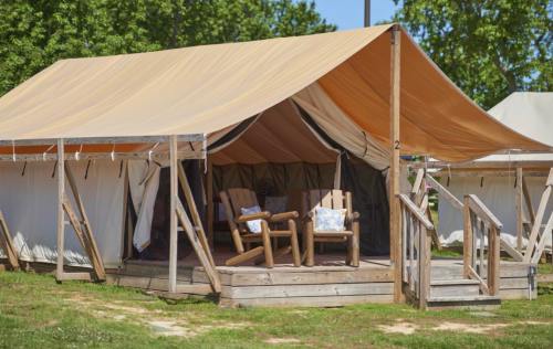 A spacious tent with a wooden deck and two chairs, set in a grassy area surrounded by trees.