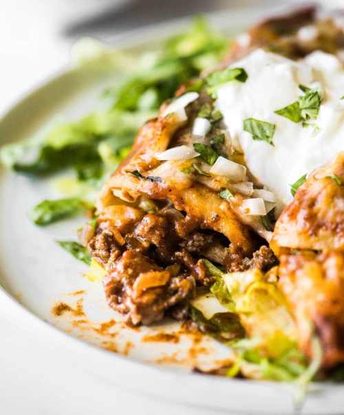 A plate of enchiladas topped with sour cream, onions, and cilantro, surrounded by fresh lettuce.