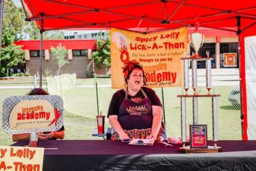 A woman laughs at a booth with a trophy, promoting a spicy lollipop event under a red tent.