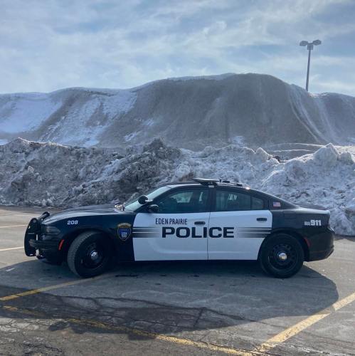 A police car parked in front of a large snow pile in a parking lot.