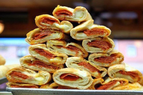 A stacked display of golden-brown pastry rolls filled with layers of pepperoni and cheese.