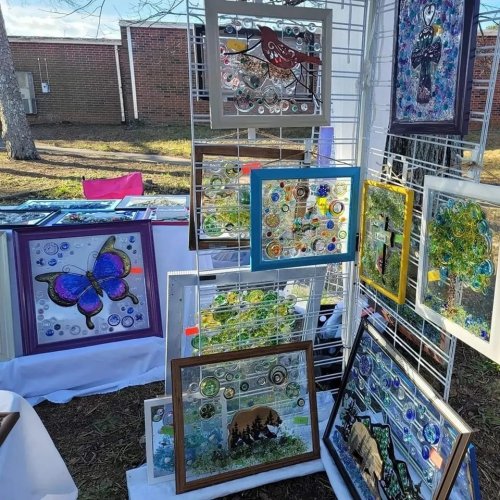 A display of colorful framed artwork featuring nature themes, including butterflies and trees, at an outdoor market.